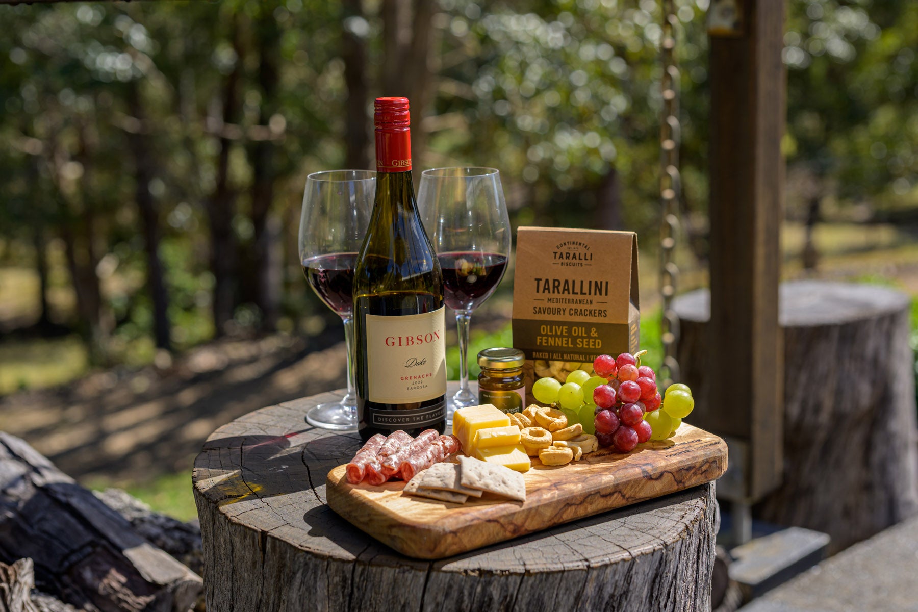 Wine bottle, glasses, and charcuterie board on a wooden stump with a natural outdoor background.