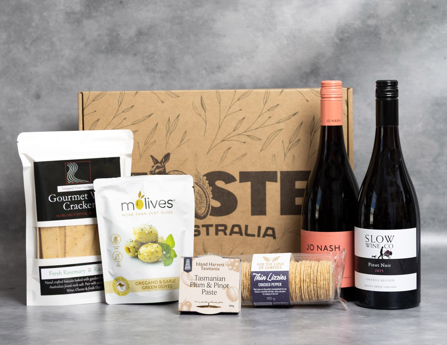 Pinot Noir Lover Hamper. Gourmet food and wine set with crackers, olives, and bottles on a gray background