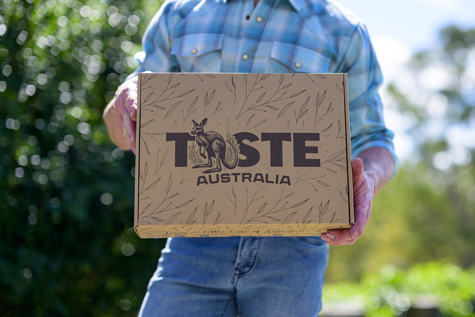 Person holding a 'Taste Australia' box outdoors with greenery in the background