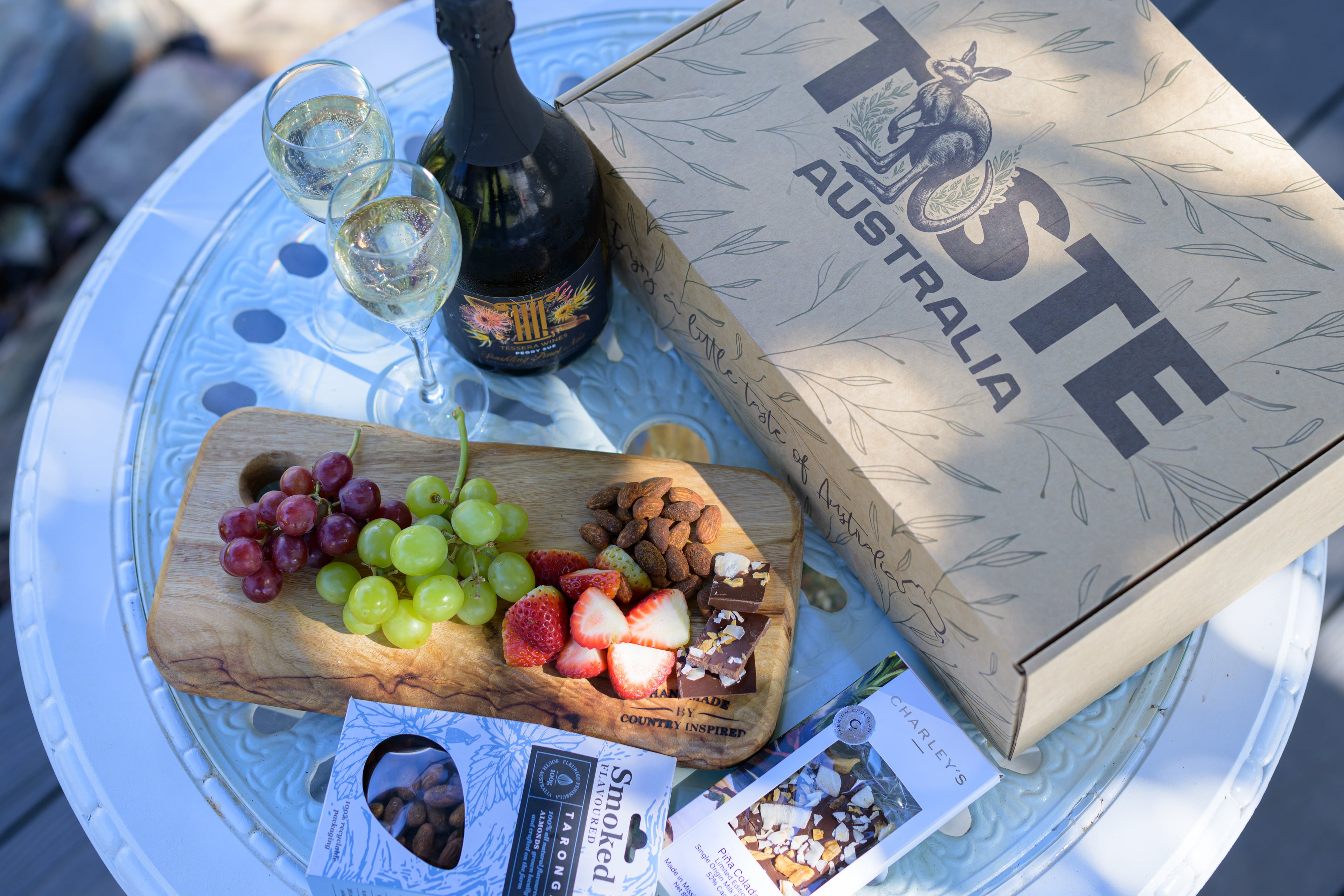 Wine bottle, glasses, and fruit platter on a table with 'Taste Australia' box.
